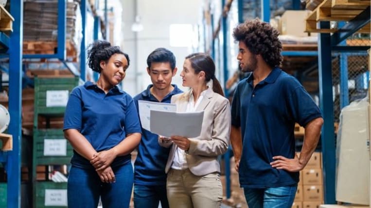 Female supervisor talking with employees in warehouse.