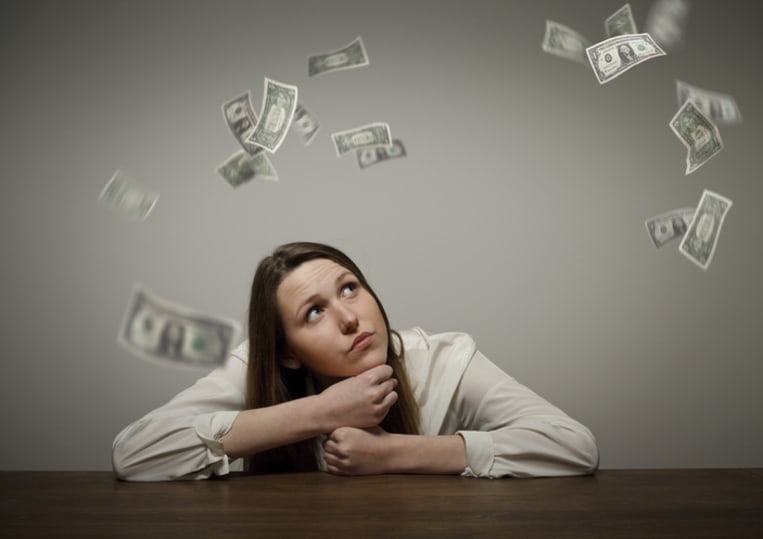 woman sitting at desk looking at money falling from the sky