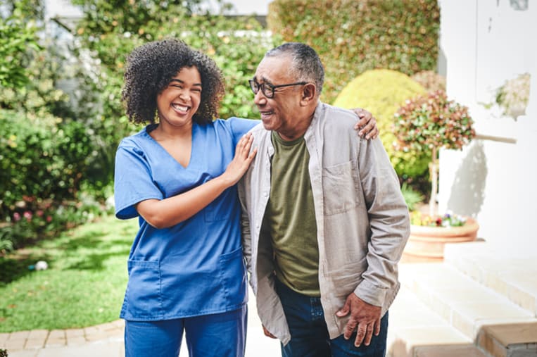 Young woman nurse smiles while putting her arm around an older man.